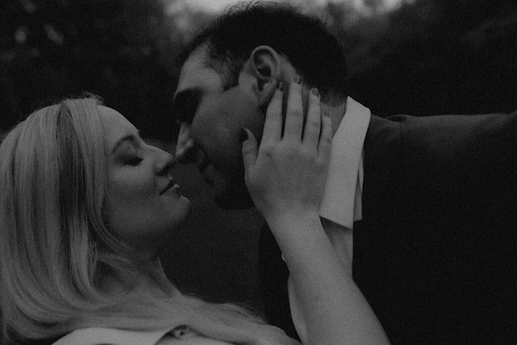 Man dips his fiancee and leans in for a kiss as she places her hand on his cheek in intimate engagement portrait. 