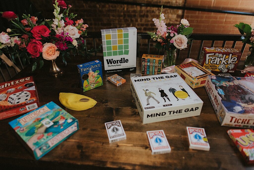 Table at reception is set with flowers in vases and board games including Wordle, Mind the Gap, Yahtzee, Farkle, Ticket to Ride, and cards for a laid back wedding reception vibe. 