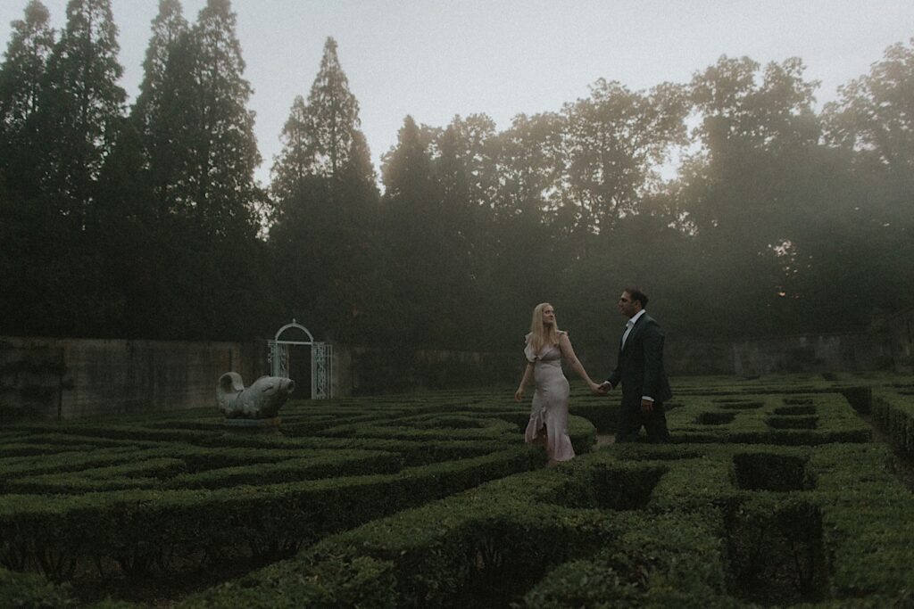 Couple walks through Allerton Park's hedge maze in romantic engagement portrait. 