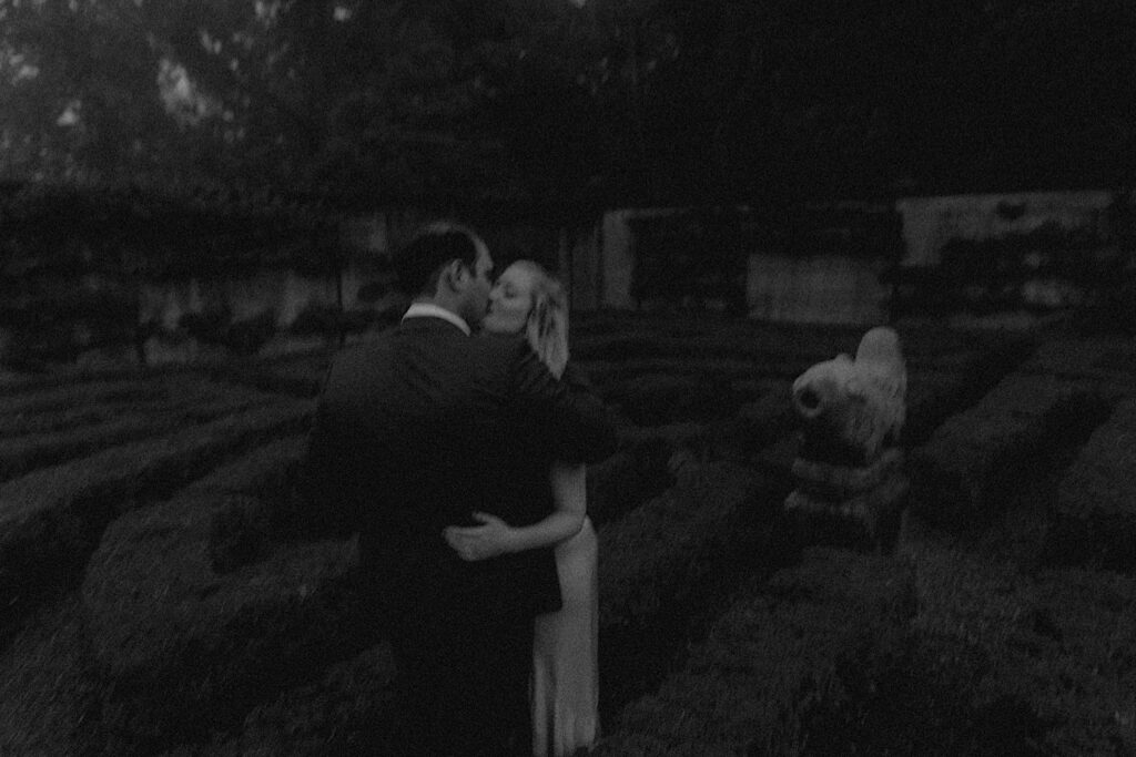 Couple kisses in fuzzy portrait in Allerton Park's hedge maze during romantic engagement session. 