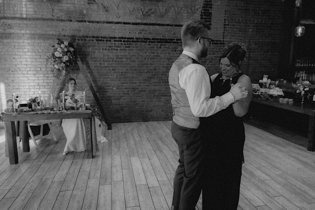 Groom and her mother dance during wedding reception at Reality on Monroe captured in a black and white portrait in Central Illinois. 