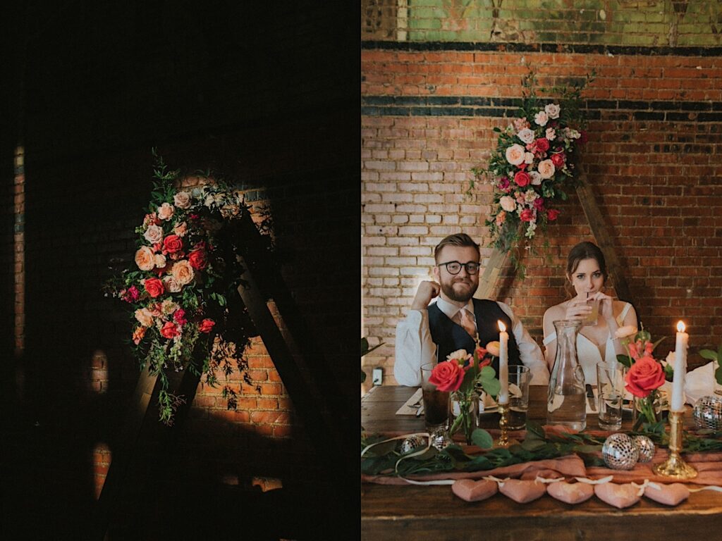 Bride and Groom sip their drinks while sitting at the head of the table during wedding reception in front of beautiful triangle flower arch.