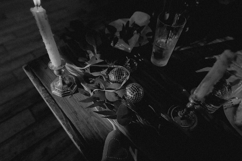 Black and white portrait of table settings of disco balls, candles in candelabras and greenery.  