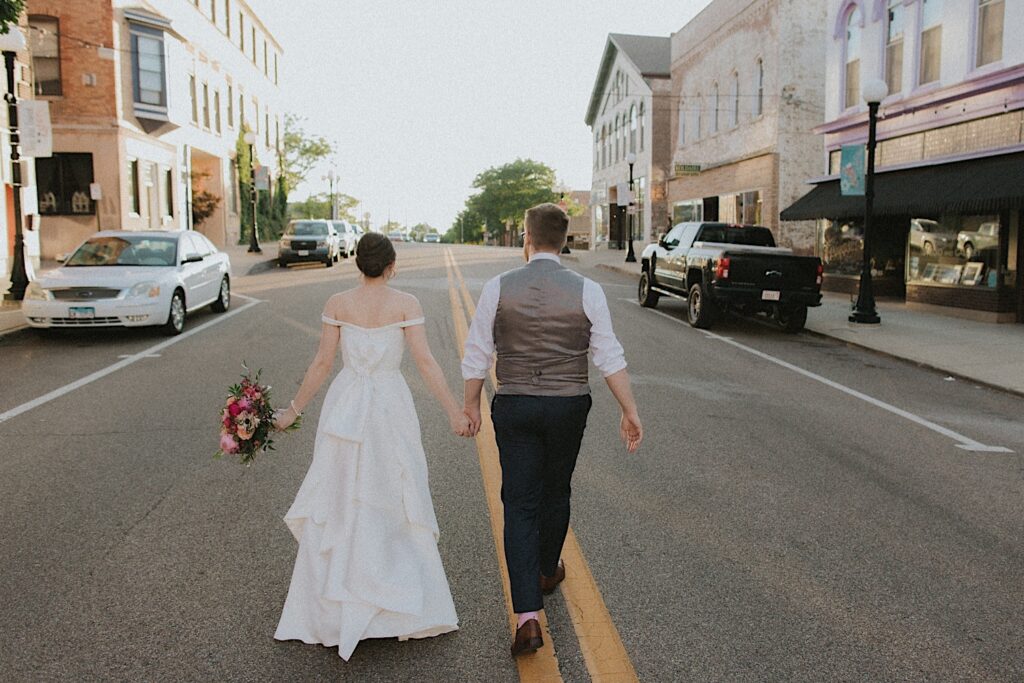 Bride and Groom walk down the with their backs facing the camera down the middle of the street in a small Central Illinois town after wedding ceremony. 