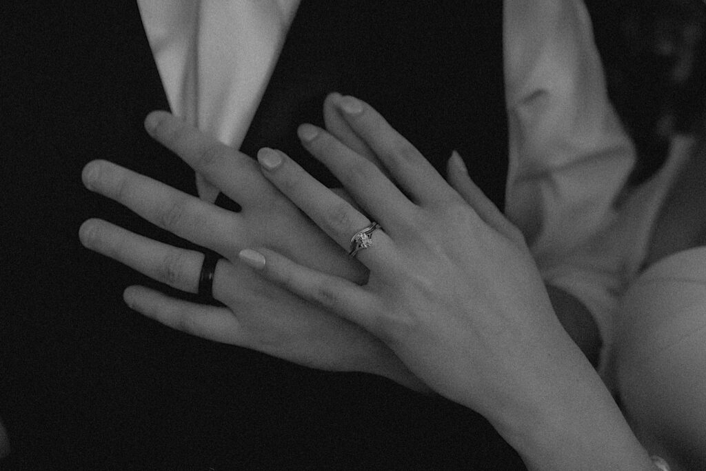 Black and White portrait zoomed in on bride and groom's hands with their engagement and wedding band rings on. 