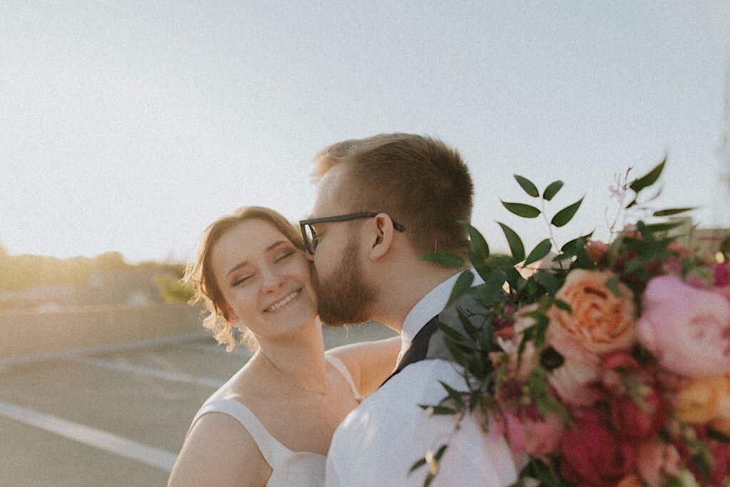 Groom kisses bride's cheek as they stand on rooftop of Reality on Monroe . 