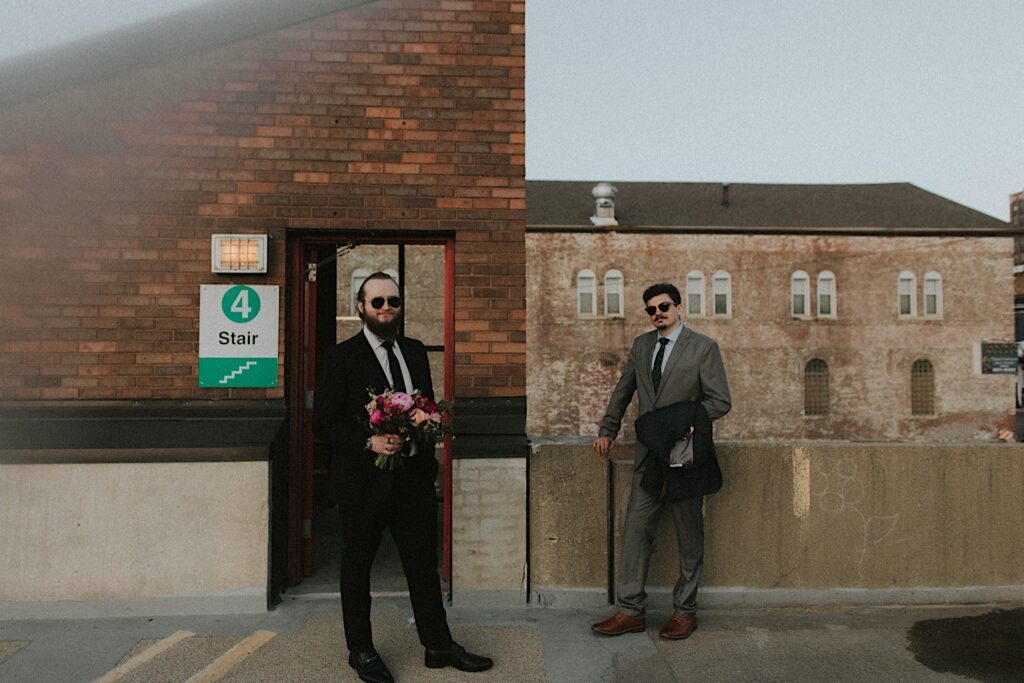 Groom and a guest stand on the roof of Reality on Monroe and pose next to stairwell in sunglasses. 