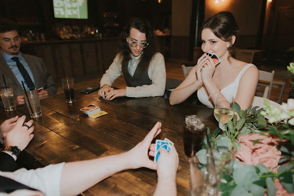 Bride keeps her Uno hand close to her face as she sits at a table around other guests during laid back wedding reception at Reality on Monroe. 