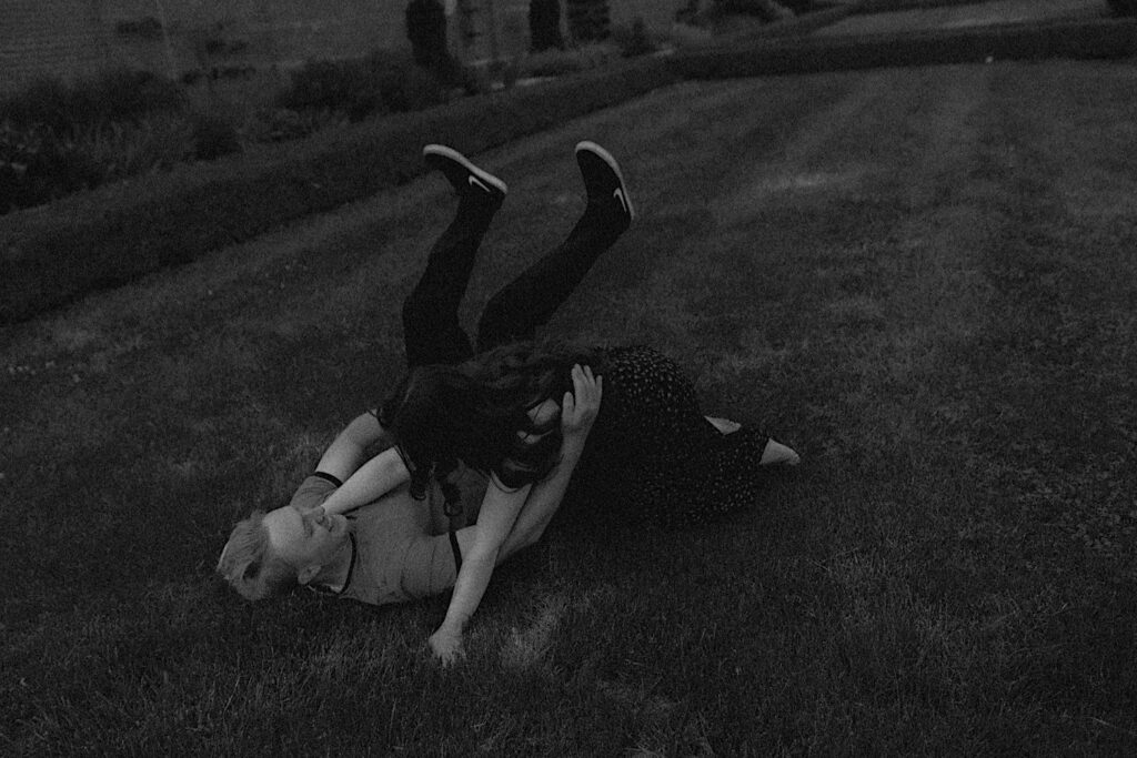 Black and white photo of a couple rolling in the grass of Allerton Park near Champaign, Illinois while having their engagement photos taken