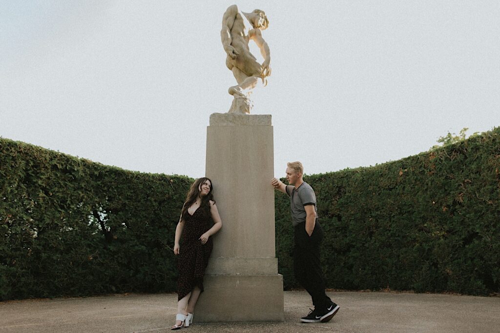 A couple pose next to a stone pillar during their engagement photos in Allerton Park of Champaign, Illinois