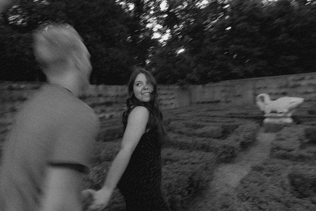 A woman looks over her shoulder and smiles at a man holding her hand while they run through Allerton Park in Champaign, Illinois while having their engagement photos taken