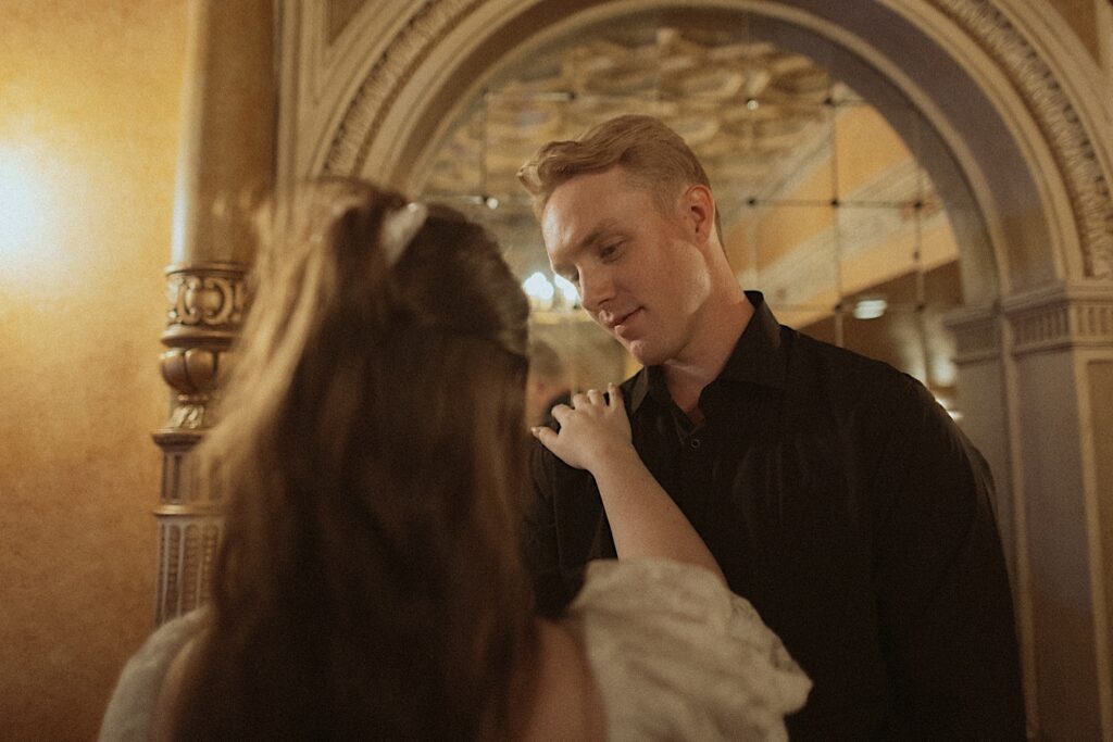 A man smiles as a woman puts her hand on his shoulder while the two have their engagement photos taking in the Virginia Theatre of Champaign, Illinois