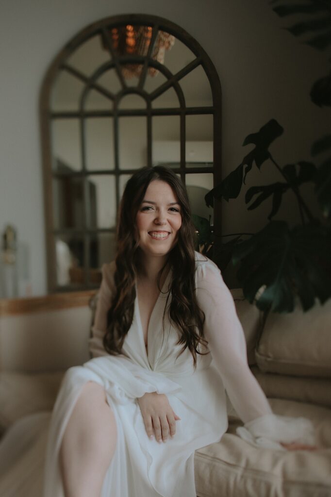 Bride sits on a white couch in a beautiful lounge smiling at the camera for a beautiful candid portrait in Illinois.