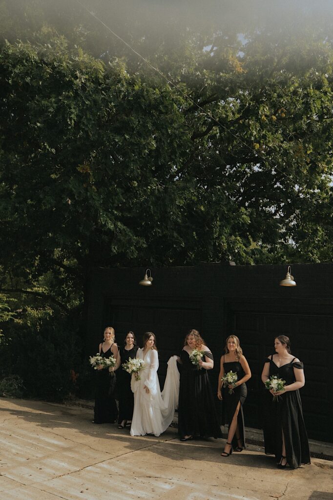 Bride and bridesmaids walk forward in front of a black garage and candidly laugh.