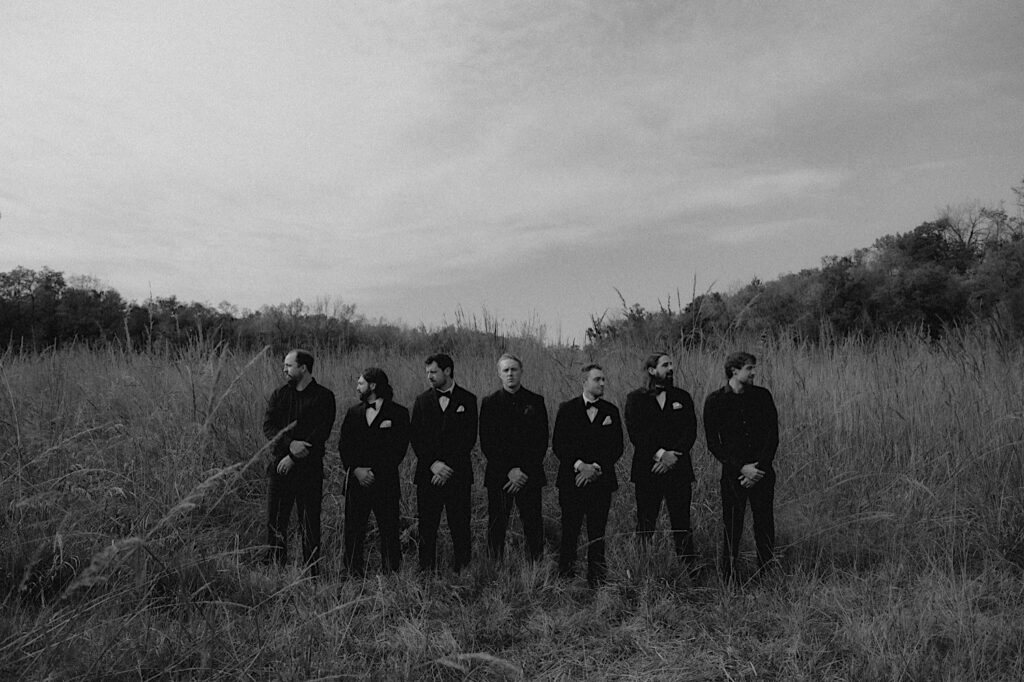 Groomsmen stand in a field and look out for a stoic portrait by Illinois wedding photographer. 