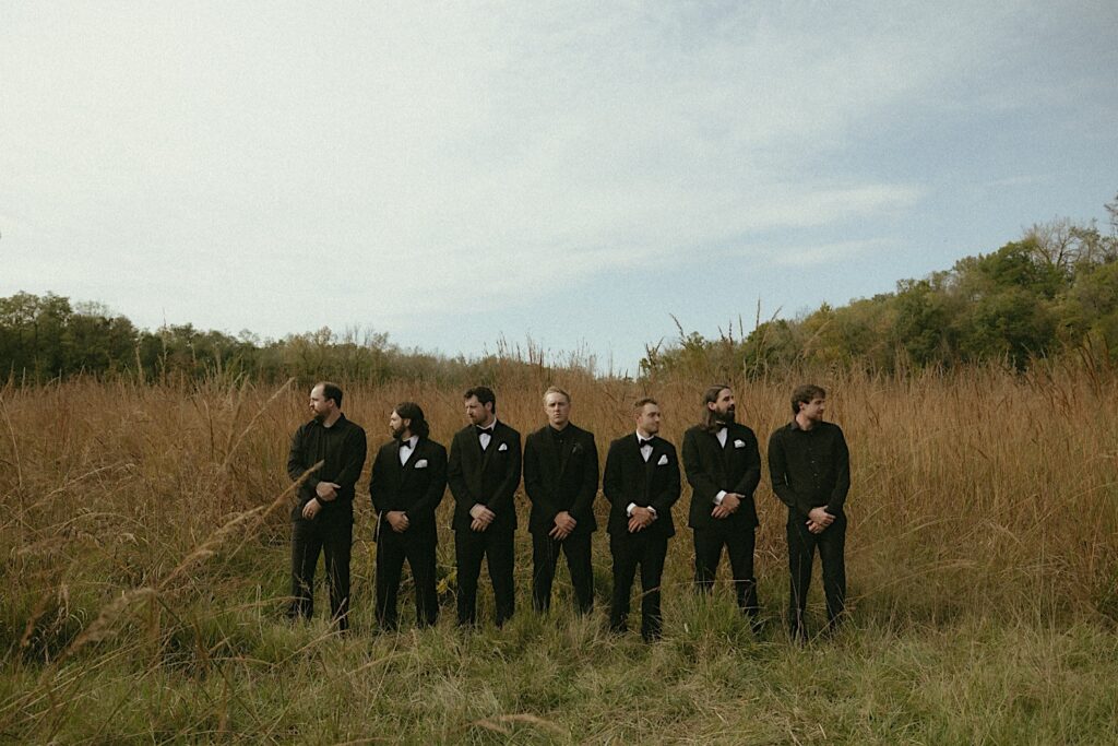 Groomsmen stand in a field and look out for a stoic portrait by Illinois wedding photographer. 