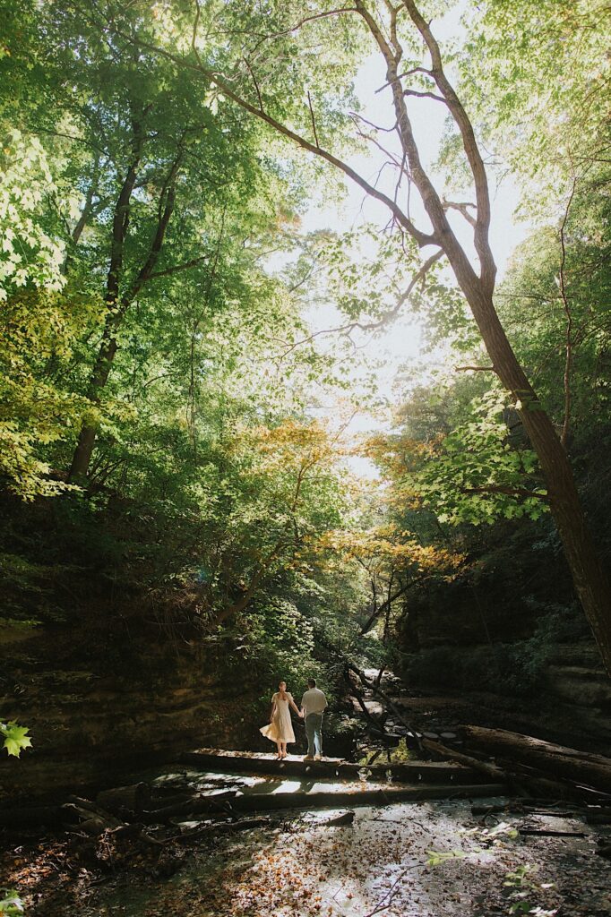 A couple stands holding one another during their engagement session in Matthiessen State Park in Central Illinois.   Light shines behind them and they're standing on a log far away from the camera.