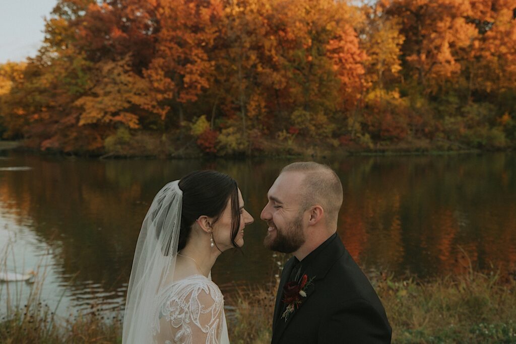 A couple holds each other close on their wedding day after their intimate elopement at Washington Park Gazebo.  Bright fall colors flood the background of the photo.