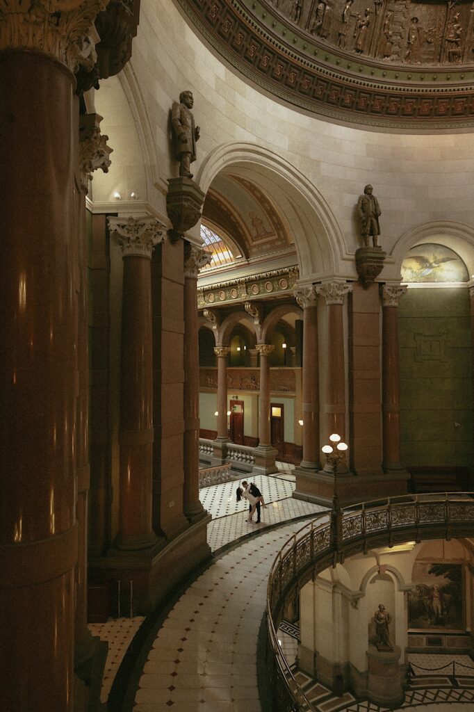 A bride and groom dance in a giant arch at the Illinois State Capitol Building.  The photographer is far away and the couple is very small in the massive marble arches that make up the space.