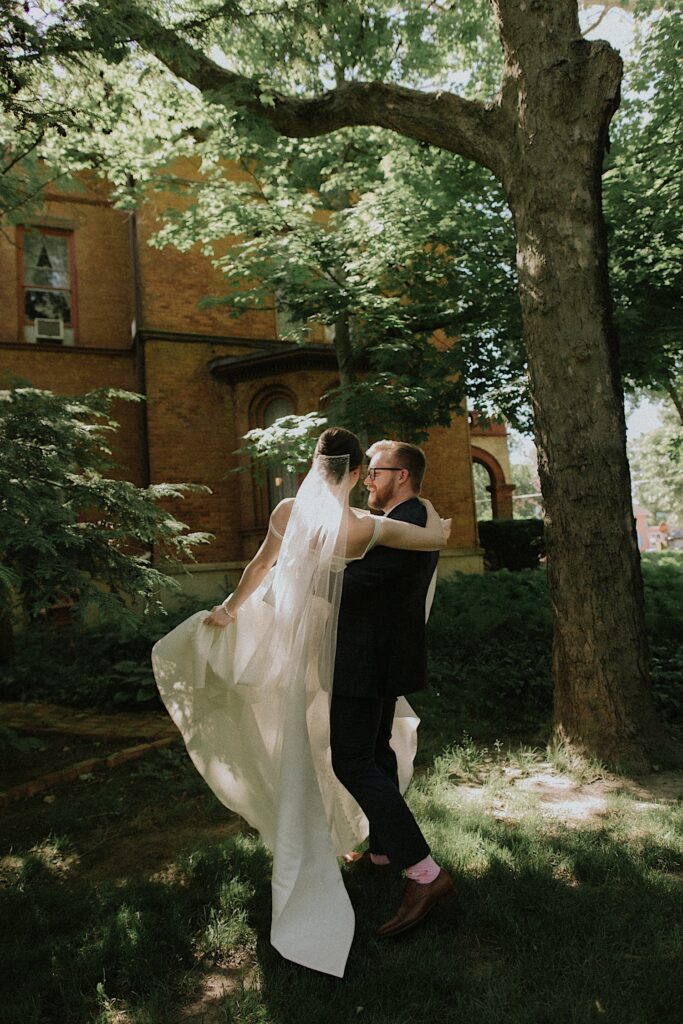 A groom picks up his bride and dances with her on the lawn outside of Vrooman mansion in the spring sun. 