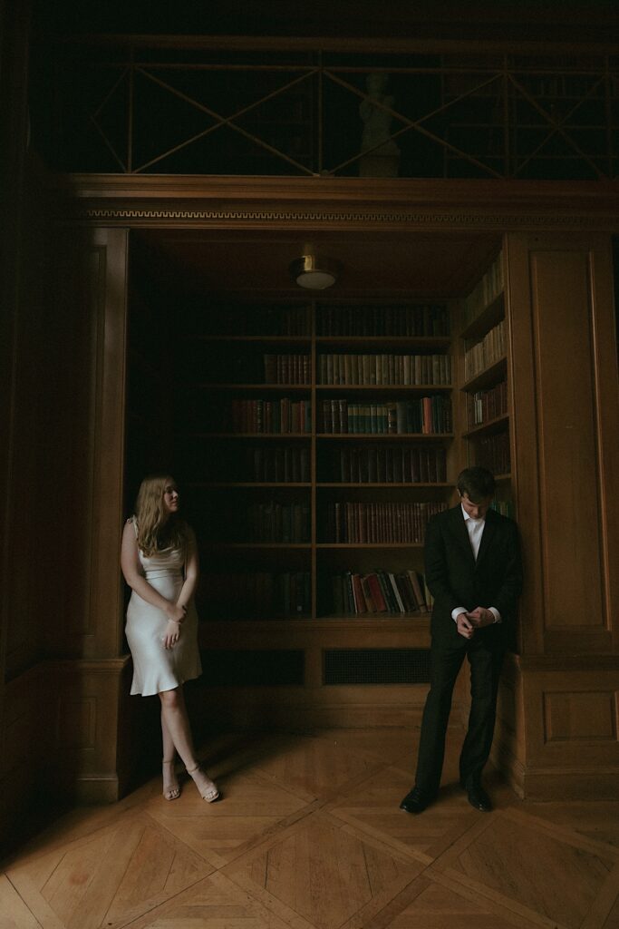 A couple stands on either side of the library in Allerton Park looking at one another.  The sun through the window is only illuminating half of their bodies. 