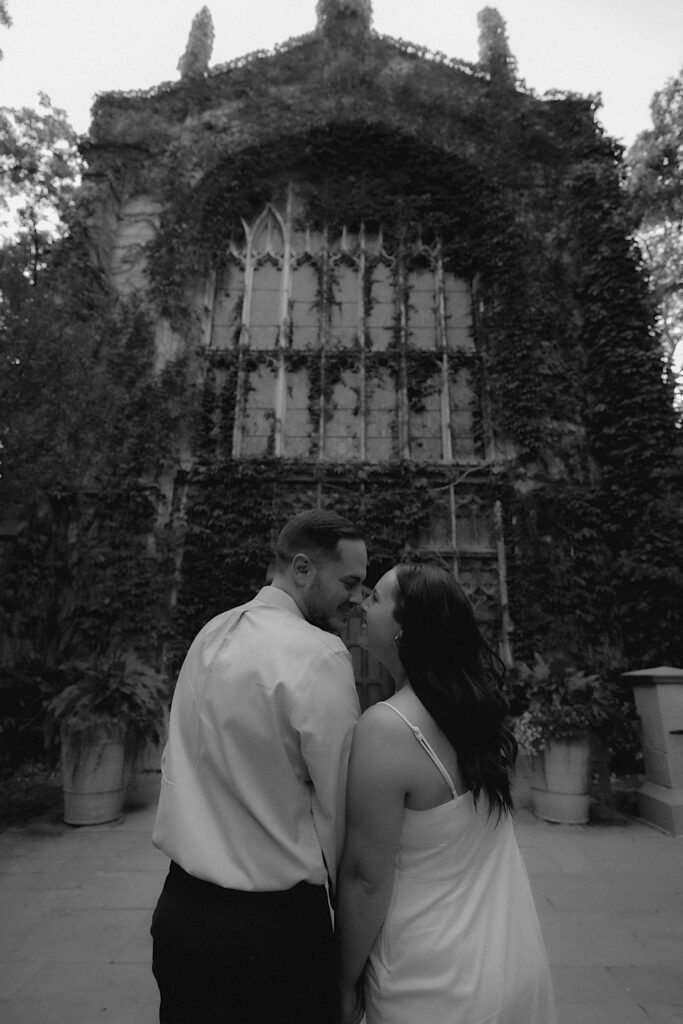 A couple stands holding hands in front of an ornate building on the University of Chicago's Campus for their engagement session