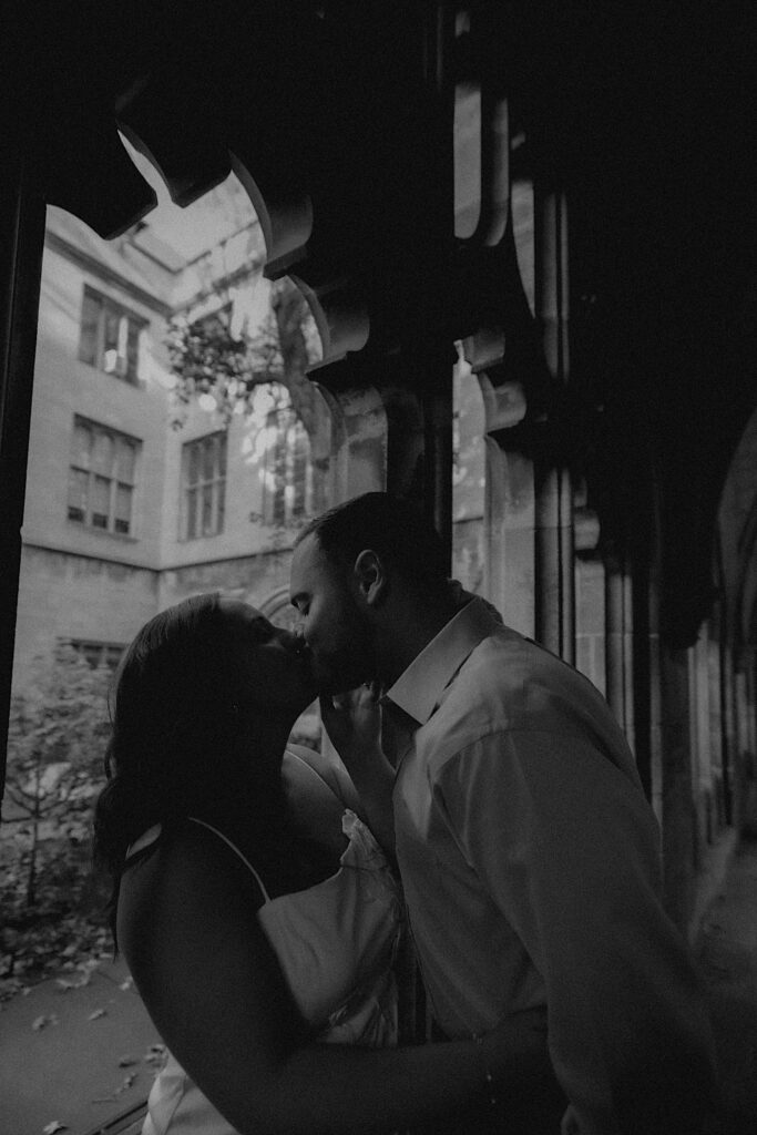 A couple stands under a covered walk way on University of Chicago's campus overlooking a courtyard. 