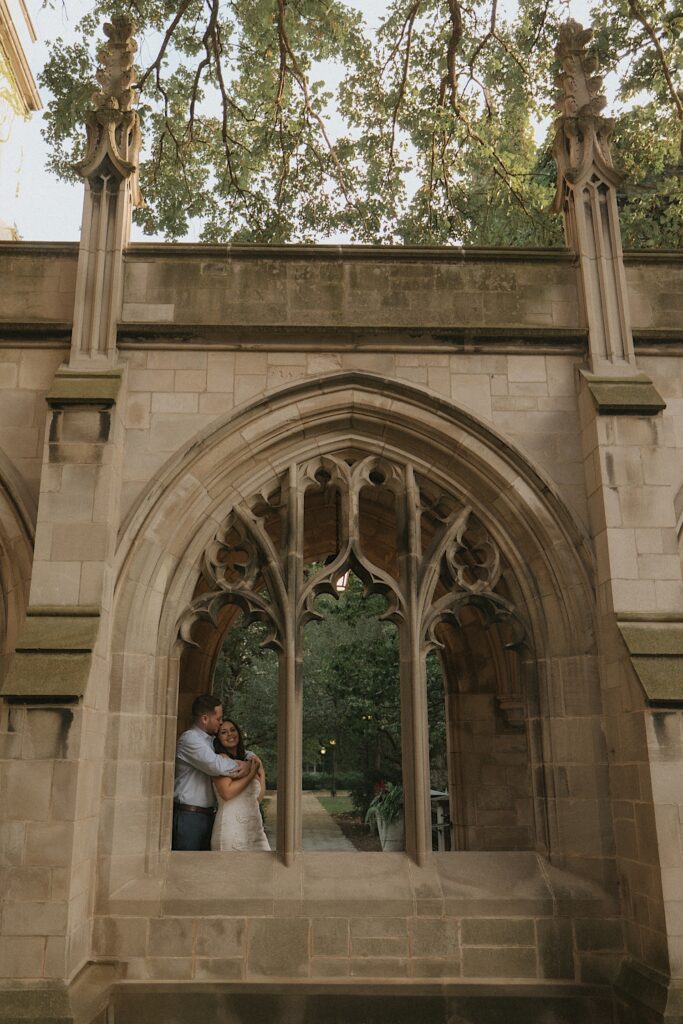 A couple stands under a covered walk way on University of Chicago's campus overlooking a courtyard. 