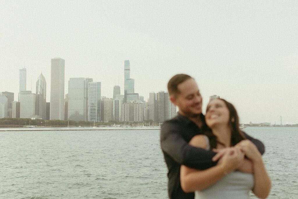 A bride and groom hold one another overlooking Lake Michigan and Navy Pier during their engagement session. 