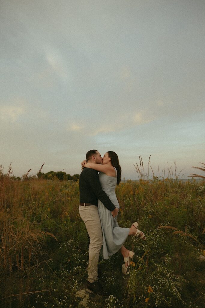 A bride and groom kiss in a field overlooking Lake Michigan during their Chicago engagement session. 