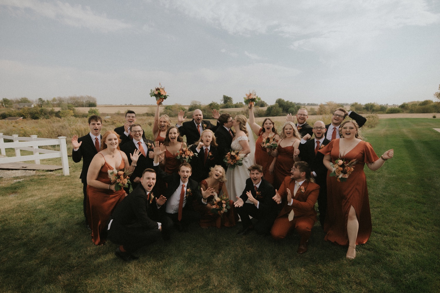 large wedding party cheers around a couple kissing on a sunny day