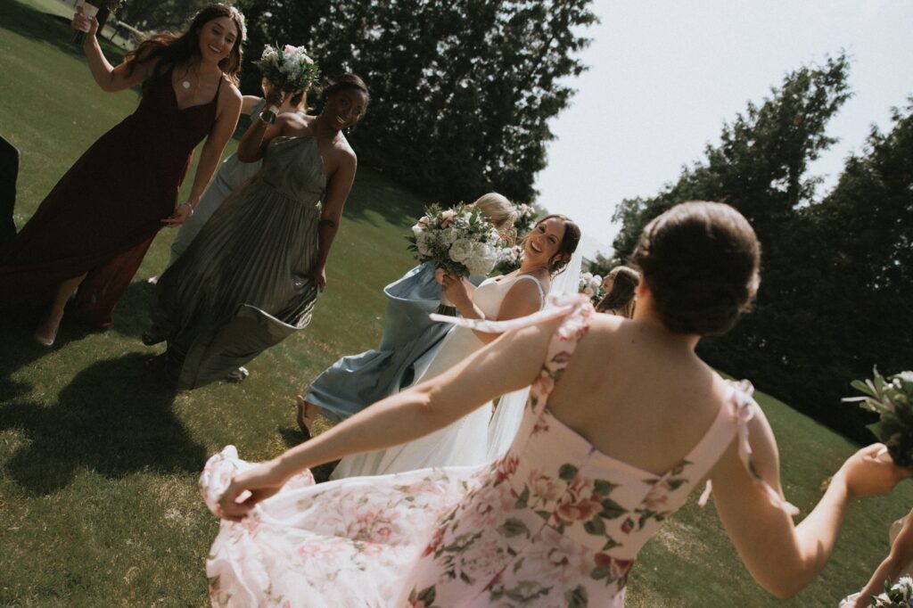 A bride dances with her bridesmaids outside of her Chicago suburbs wedding venue.  The bridesmaids wear multicolored wedding dresses. 