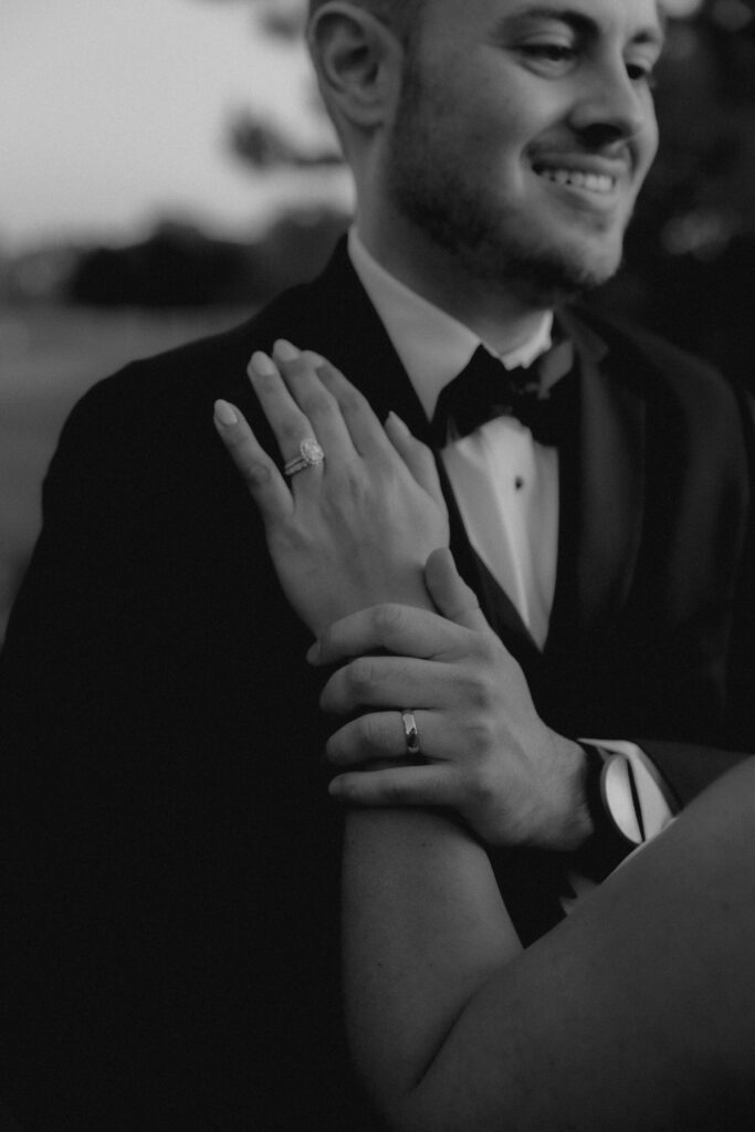 A bride and groom hold one another on their wedding day at the Chicago suburbs wedding venue the Chevy Chase Country Club.  In the photo they show off the grooms black tie attire and their wedding rings. 