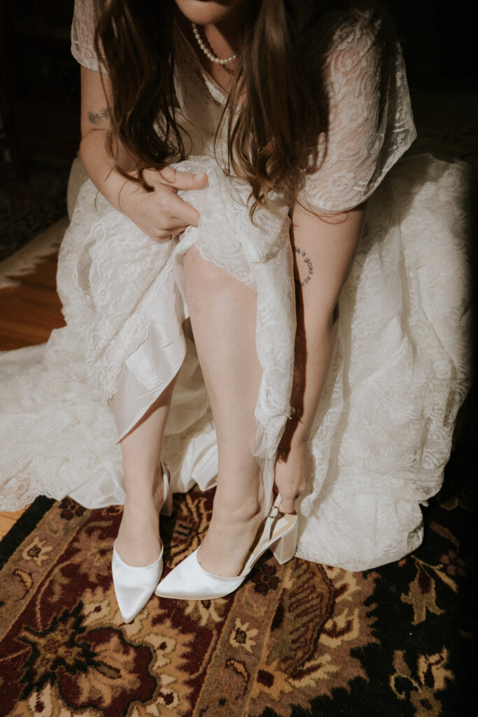 bride puts on her white heals in preparation of her greenhouse wedding day